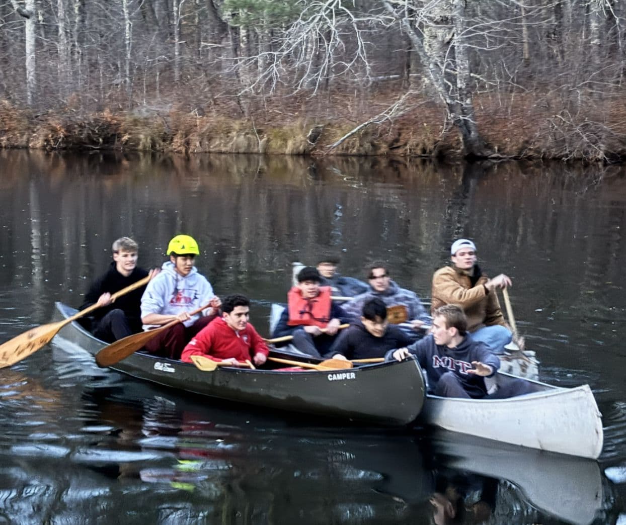Two canoes of brothers paddling down a wooded river.