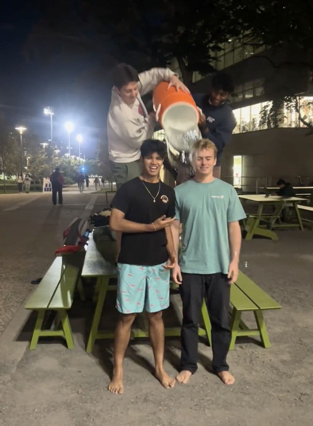 Brothers being doused with a bucket of water at an evening charity event.