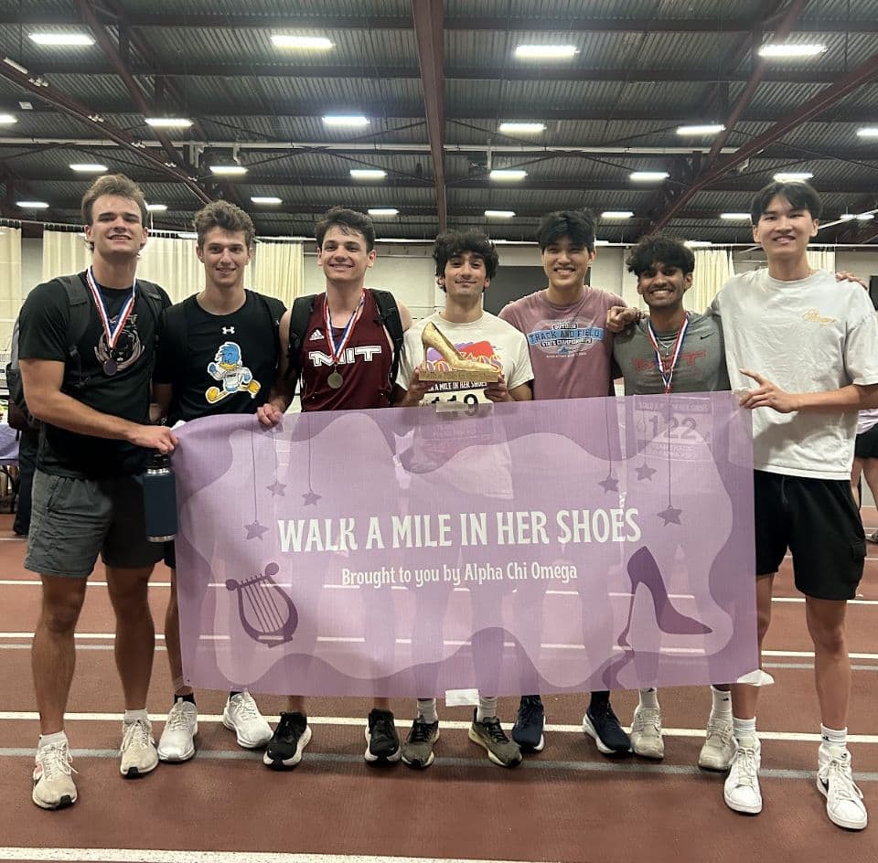 Brothers with medals holding the Walk a Mile in Her Shoes banner on the track.