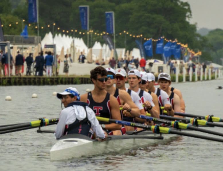 An MIT eight rowing past the tents at a regatta.