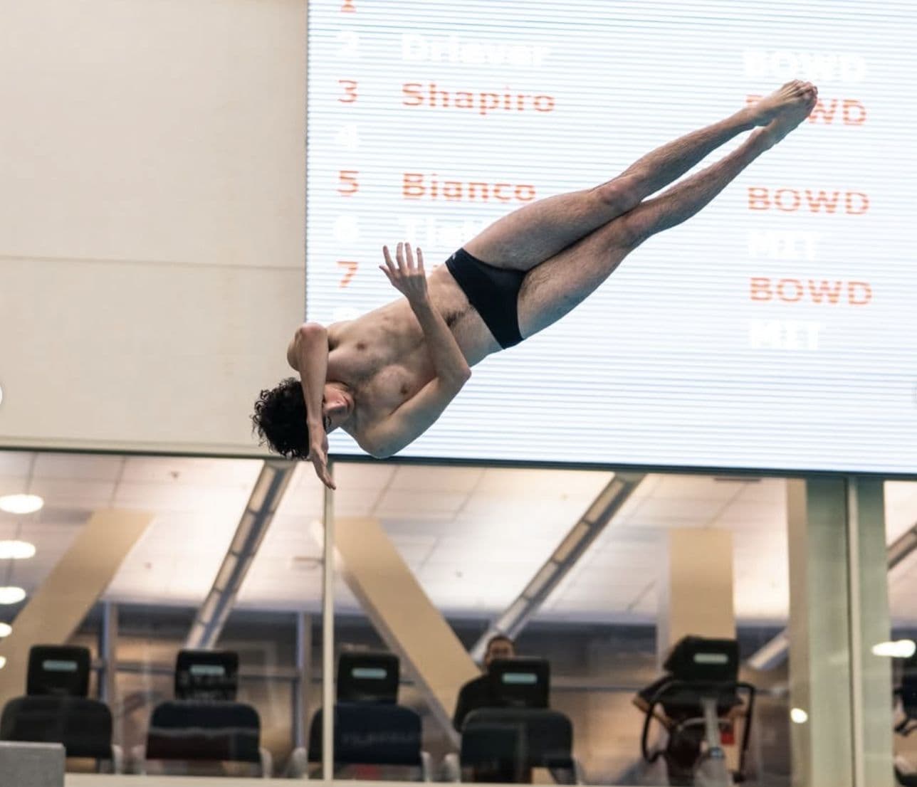 An MIT diver in a tucked somersault above the board.